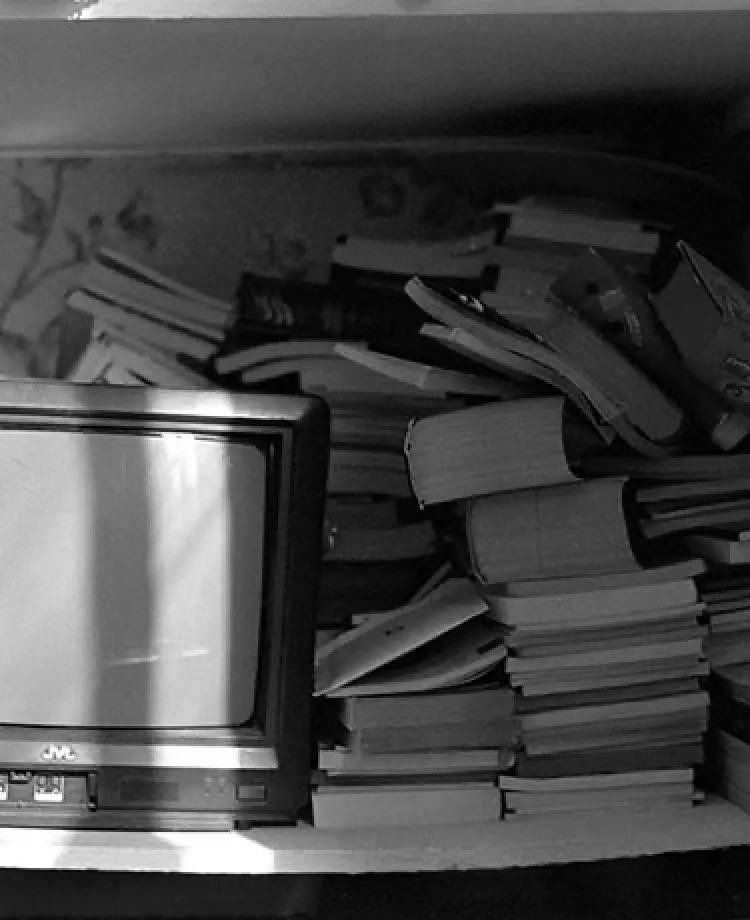 アナログテレビの右横に本が乱雑に積み上げられている様子