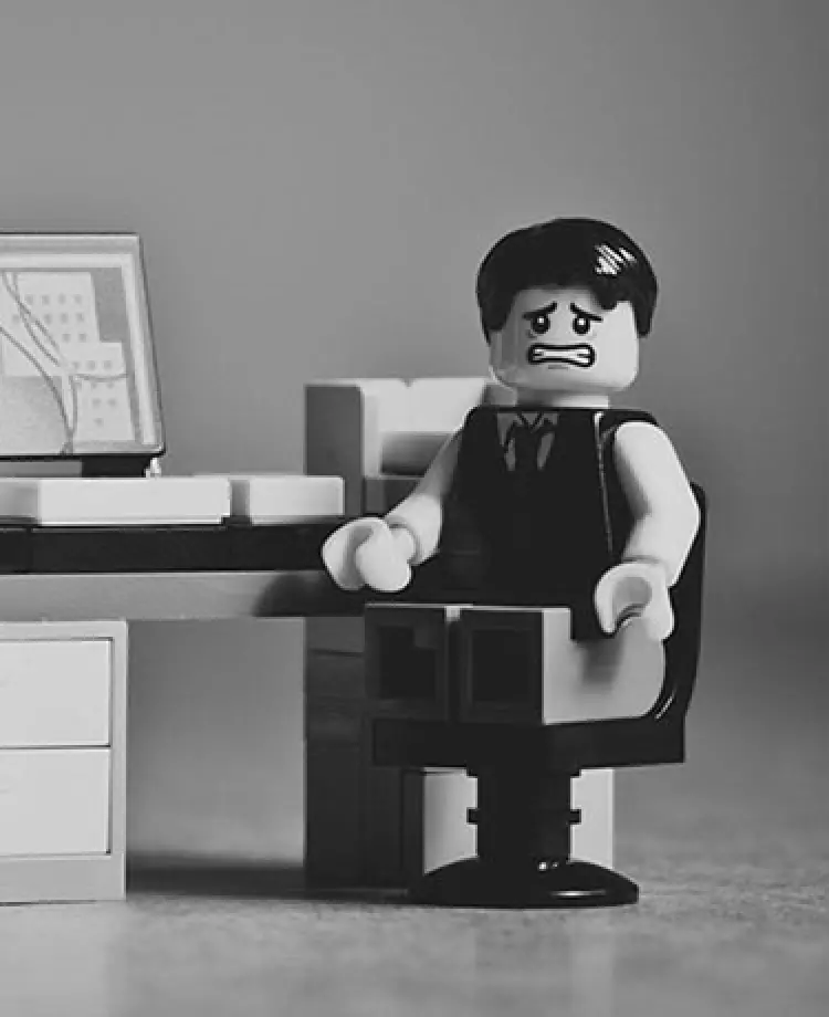 PCの前に座るスーツを着たレゴ人形が、こちらを困った顔で見つめる様子