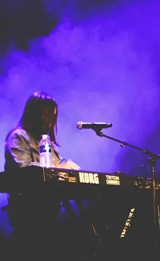 暗闇に紫いろのスモークが焚かれる中、シンセサイザーを演奏するミュージシャンの様子。